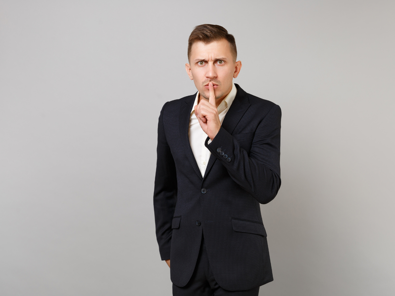 Homme d'affaire avec un doigt sur la bouche demandant le silence.