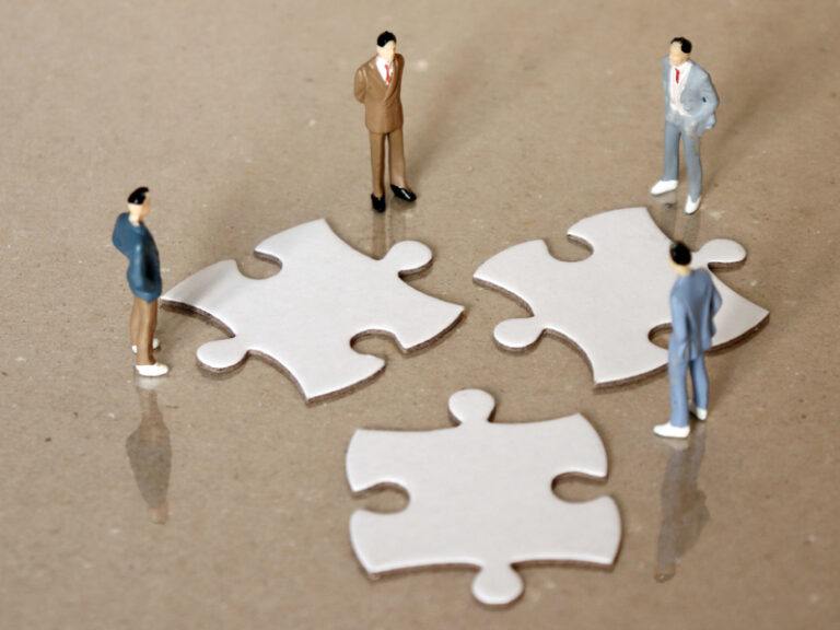 Quatre hommes d'affaires autour de trois pièce de puzzle, songeant à une fusion.