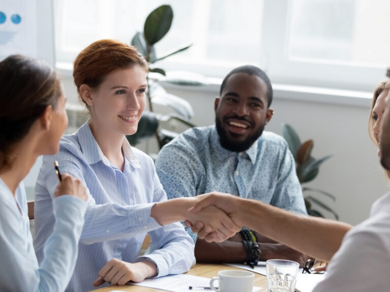 Plusieurs personnes en tenue de travail autour d'une table, deux d'entre elles se serrent la main.