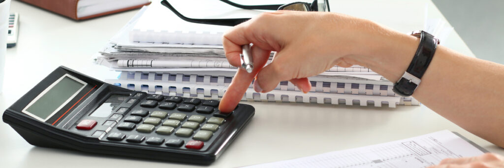 La main d'une femme tapant sur une calculette posée sur une table.
