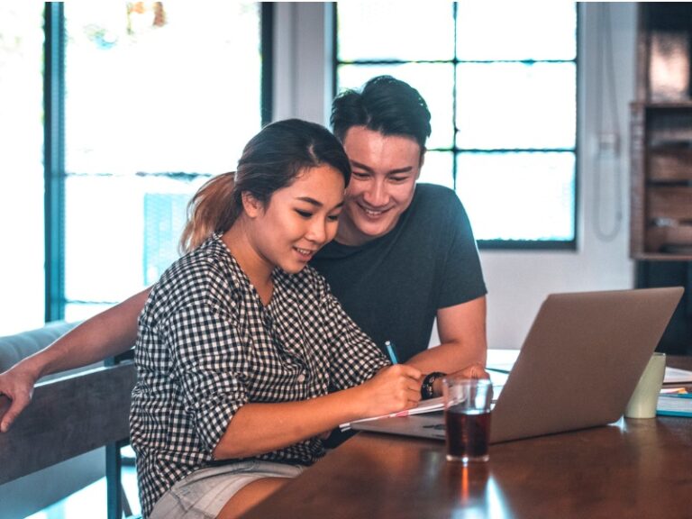 Un couple devant un ordinateur dans une maison. Ils ont l'air heureux.
