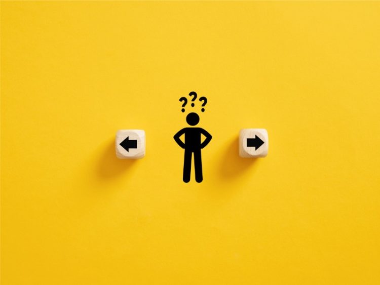 Prise de décision et choix de la bonne voie. Confusion quant au choix de la direction à prendre. Stickman avec des points d’interrogation debout entre les cubes en bois avec des symboles de flèche.