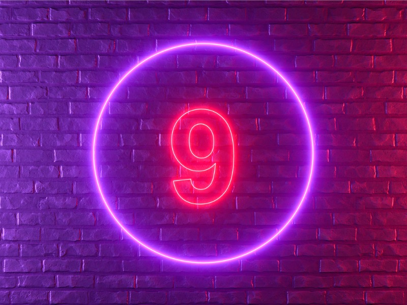 Numéro 9 avec éclairage au néon brillant sur un mur de briques noires.