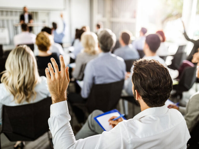 Une salle remplie de personnes prenant des notes en face de quelqu'un qui semble donner une conférence.