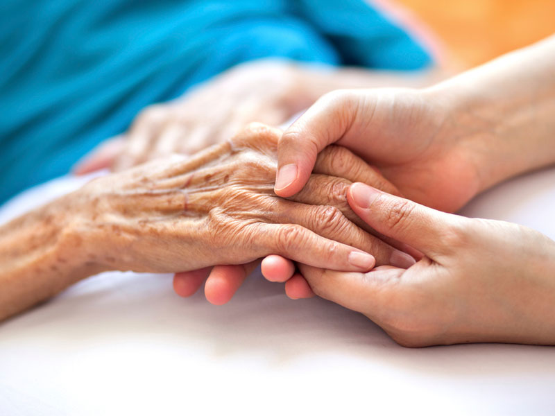 Une jeune femme tenant la main d'une femme âgée qui est couchée dans un lit.