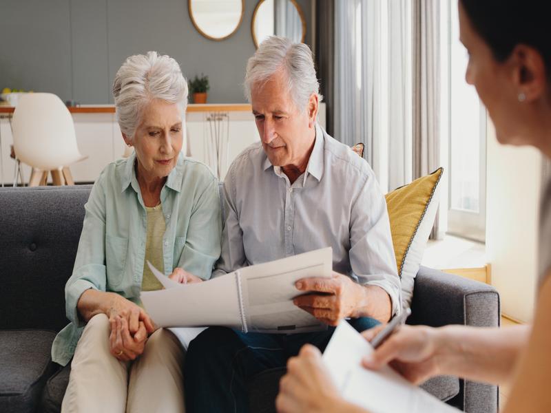 Couple de personnes âgées consultant des documents financiers avec une conseillère à domicile.