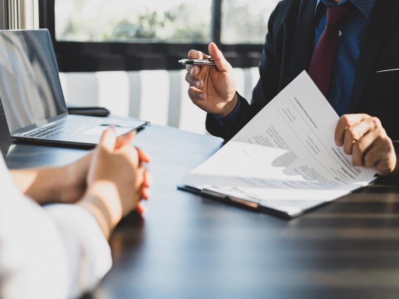 Rencontre professionnelle entre un conseiller (en complet) et un client, avec des documents financiers sur la table.