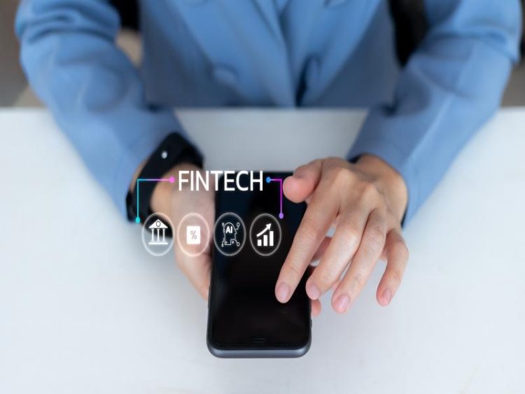 Gros plan sur une personne en veste bleue utilisant un smartphone. Le mot FINTECH apparaît en surimpression, accompagné d’icônes symbolisant la banque, les taux, l’intelligence artificielle et la croissance.