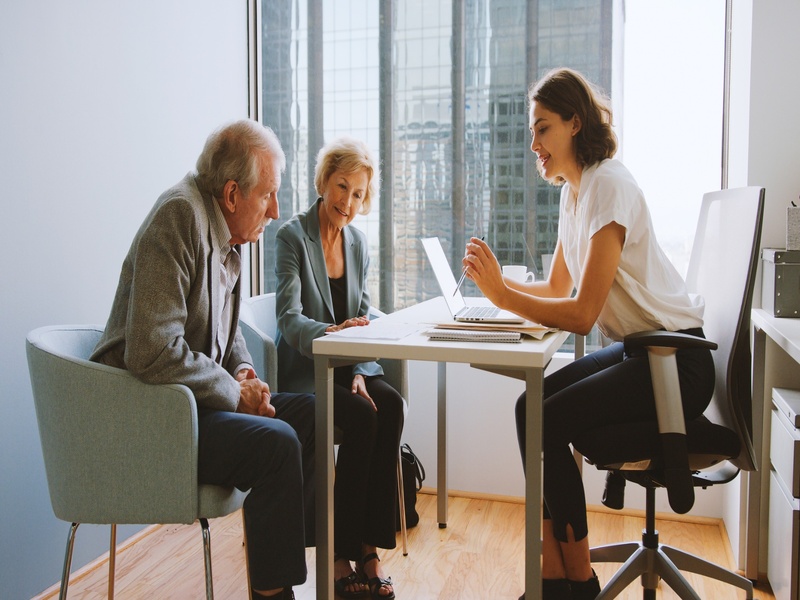 Conseillère discutant avec un couple de personnes âgées, représentant la gestion patrimoniale et le conseil personnalisé.