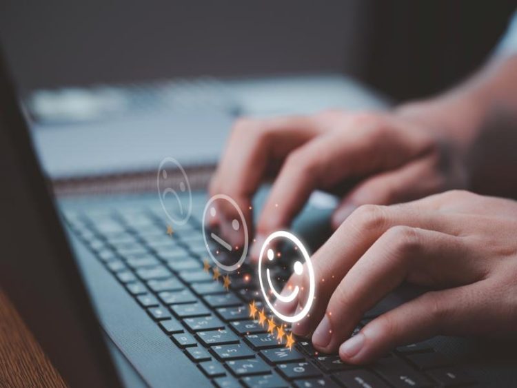 Mains tapant sur un clavier d’ordinateur portable avec des icônes de satisfaction et des étoiles symbolisant l’expérience utilisateur et l’évaluation en ligne.