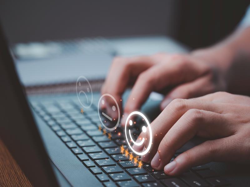 Mains tapant sur un clavier d’ordinateur portable avec des icônes de satisfaction et des étoiles symbolisant l’expérience utilisateur et l’évaluation en ligne.