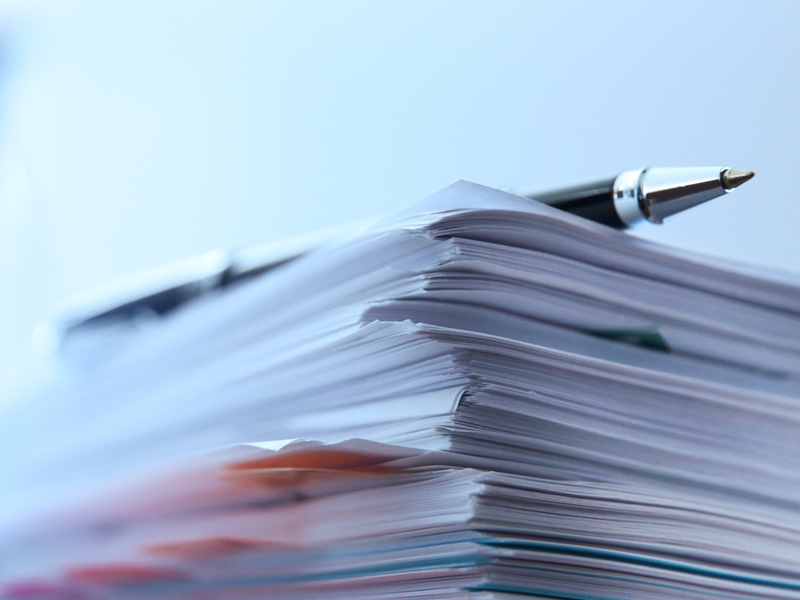 Une pile de documents administratifs illustre le traitement et la gestion de dossiers.
