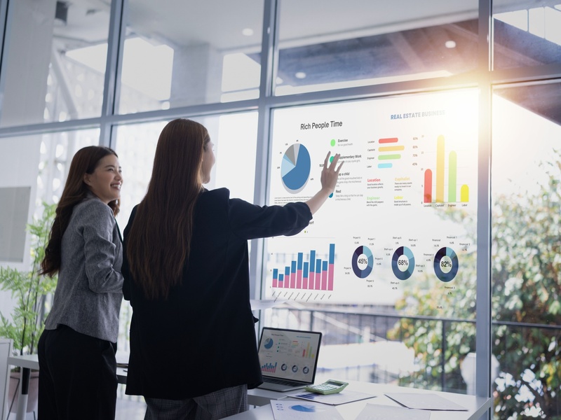 Deux professionnelles analysent des tableaux de bord et des indicateurs de performance lors d'une présentation.